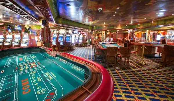 Interno luminoso di un casinò su una nave da crociera, con tavoli da gioco, slot machine e atmosfera vivace in stile vacanza.
